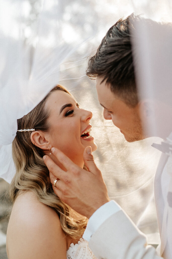 Bride and Groom laughing under a veil with their Scenic Rim Wedding Photographer. 